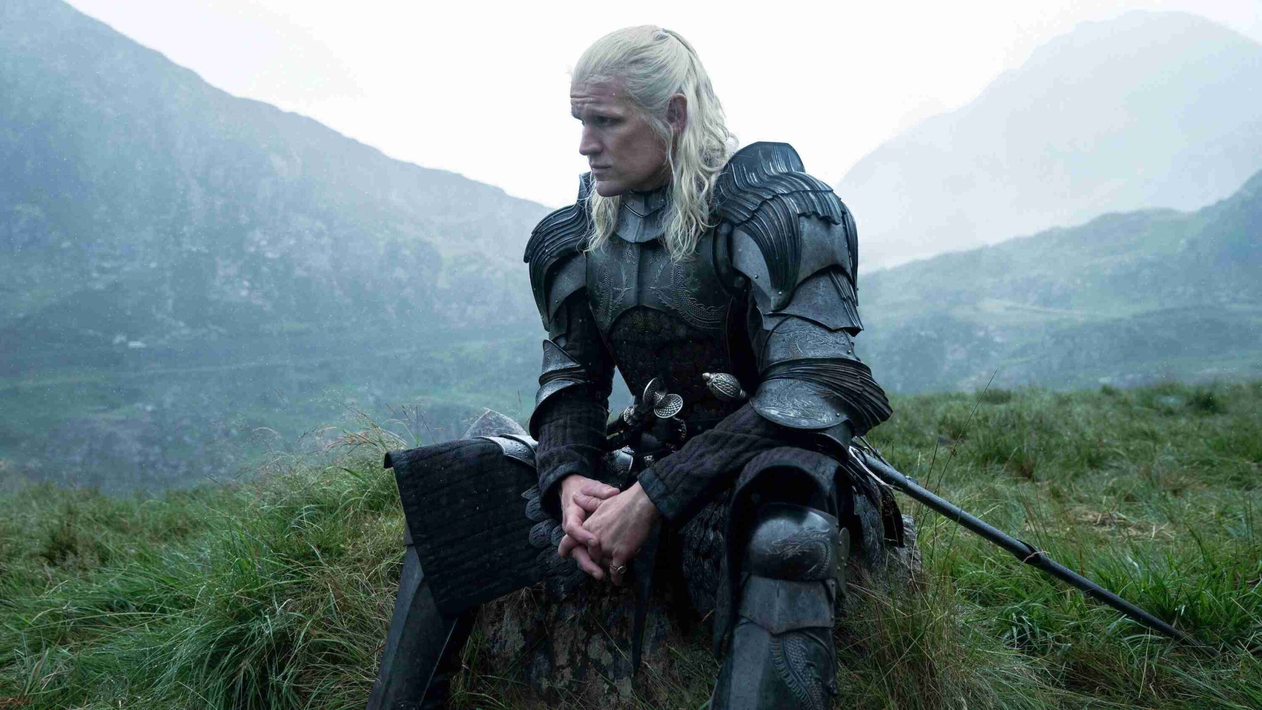Knight in Dark Ornate Armor Sitting in a Grassy Field with Misty Mountains in the Background