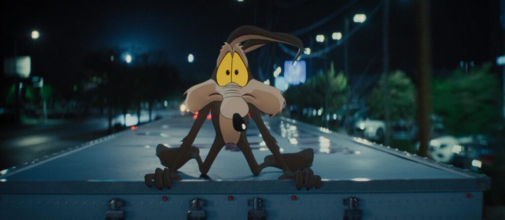 Cartoon Coyote Crouches on the Back of a Truck on a Dark City Street at Night with Blurred Streetlights in the Background