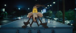 Cartoon Coyote Crouches on the Back of a Truck on a Dark City Street at Night with Blurred Streetlights in the Background