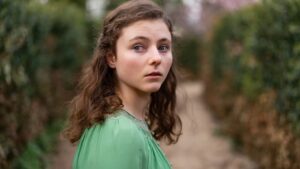 Portrait of a Young Woman with Wavy Brown Hair in a Green Blouse Standing on a Garden Path and Looking Toward the Camera