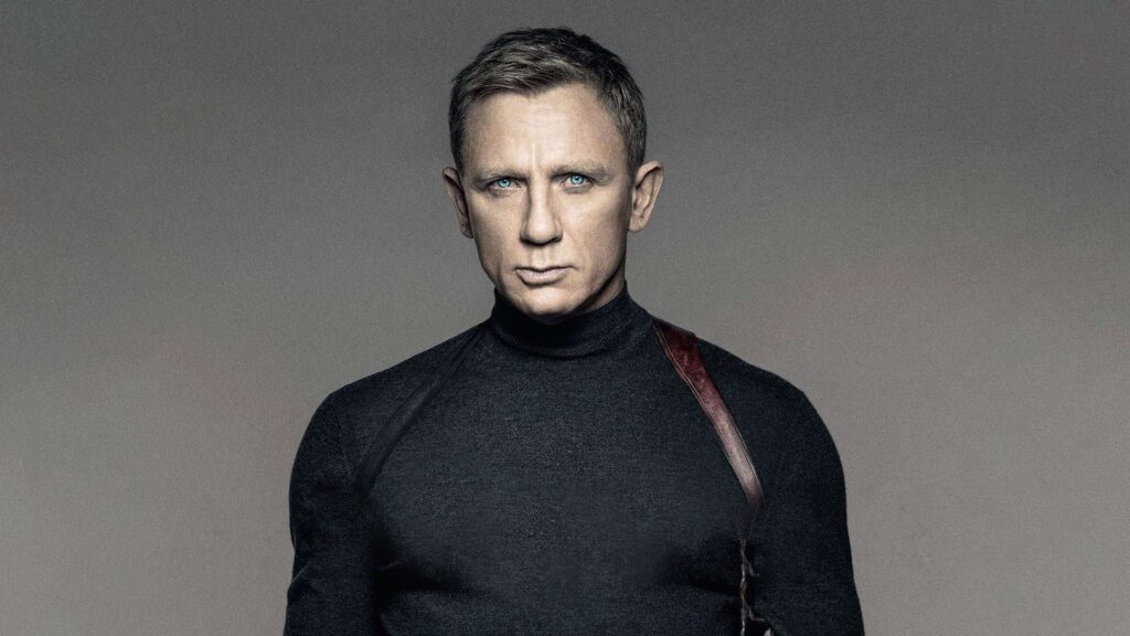Man with a Stern Expression Wearing a Black Turtleneck and a Diagonal Leather Strap Across His Chest Against a Gray Gradient Background