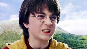 Person with Short Dark Hair and Round Glasses Making a Grimace Outdoors with Green Hills and Blue Sky Behind