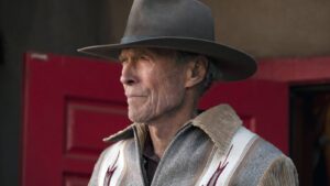 Older Man Wearing a Wide brimmed Gray Hat and a Tanandgray Poncho Standing in Front of a Red Door