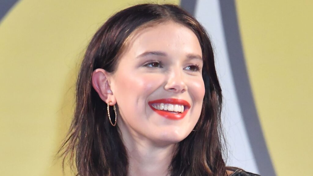 Close up of a Smiling Woman with Dark Hair Red Lipstick and Gold Hoop Earrings Against a Yellow Backdrop