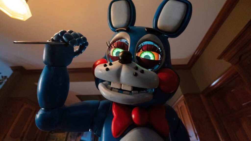 Blue Animatronic Bunny Raises a Knife Looking Toward the Viewer with Glowing Green Eyes Red Bowtie Indoors in a Kitchen like Room