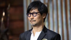 Man with Black Hair and Blue rimmed Round Glasses Wearing a White Shirt and Dark Blazer Looking to the Side