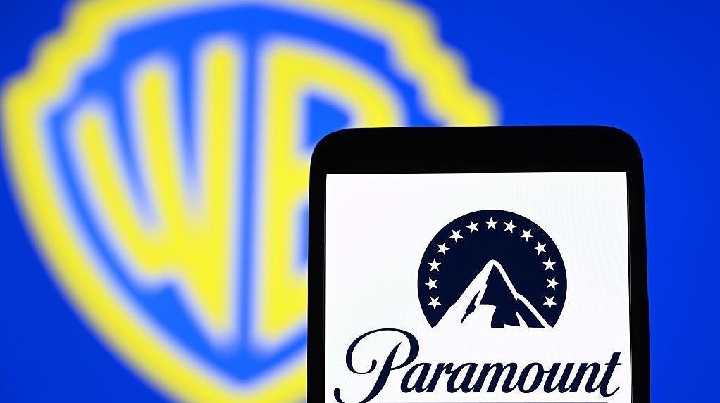 Tablet Displaying the Paramount Logo with a Blurred Blue Background and a Yellow Warner Bros Emblem Behind It
