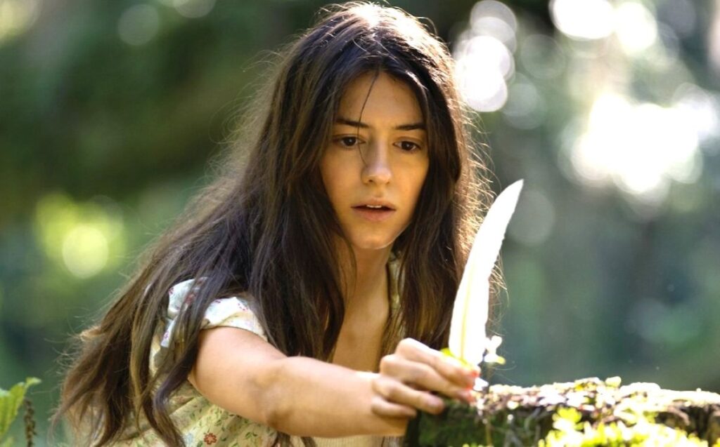 Woman with Long Dark Hair in a Floral Top Holding a Curved Knife Outdoors Beside a Mossy Surface