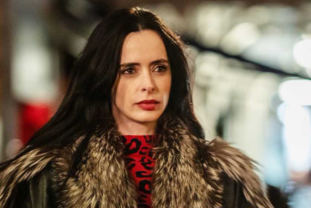 Woman with Long Dark Hair Wearing a Fur Coat over a Red Leopard print Top Looking Thoughtful in a Blurred Indoor Setting