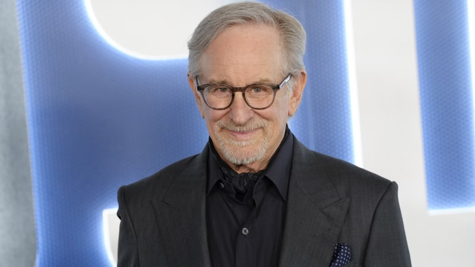 Mature Man with Gray Hair and Glasses in a Dark Suit Smiling at the Camera