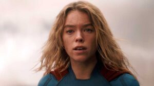 Close up of a Blond Woman in a Blue Superhero Suit with a Red Cape Looking Determined Outdoors
