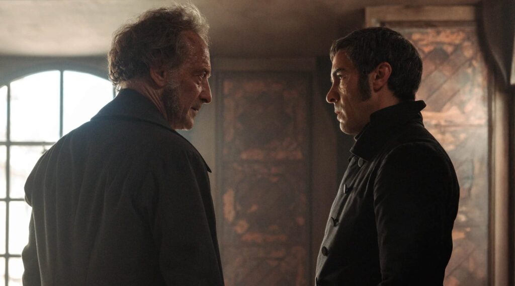 Two Men Stand Face to face in a Dim Smoky Room One with Gray Hair and the Other with Dark Hair Conveying a Tense Confrontation