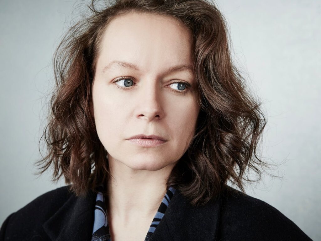 Woman with Shoulder length Wavy Brown Hair and Blue Eyes Wearing a Dark Coat Looking to Her Left