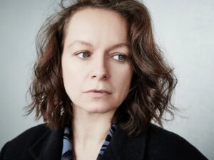 Woman with Shoulder length Wavy Brown Hair and Blue Eyes Wearing a Dark Coat Looking to Her Left