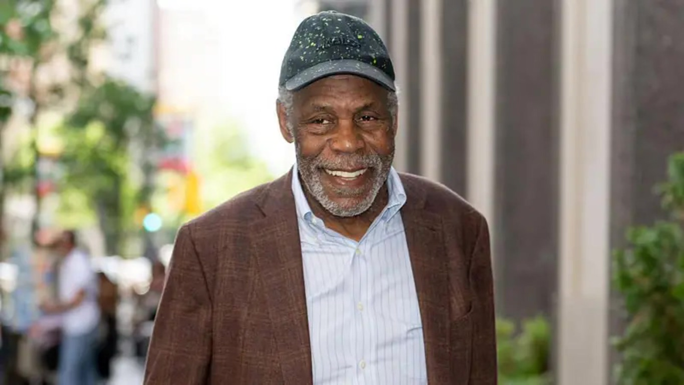 Smiling Older Man in a Brown Blazer and Light Blue Striped Shirt Wearing a Black Cap Walking on a City Sidewalk