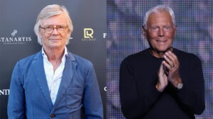 Two Older Men at an Event Left Man with Gray Hair and Glasses in a Blue Blazer Right Man in a Black Shirt Clapping on a Stage Backdrop