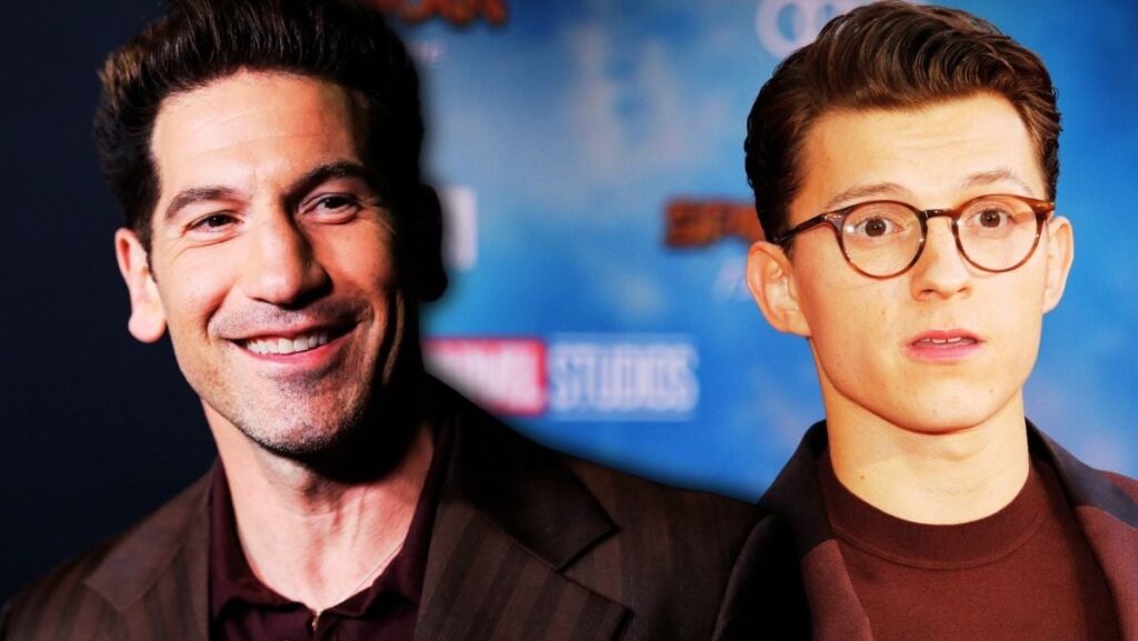 Two Men in Dark Jackets Pose Together at a Blue Backdrop One Smiling Warmly the Other Wearing Round Glasses the Setting Suggests a Studio Event or Premiere Backdrop