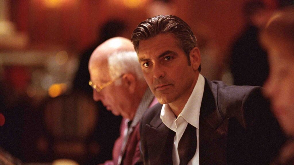 Man in a Dark Suit and White Shirt at a Dimly Lit Formal Event Looking Toward the Camera
