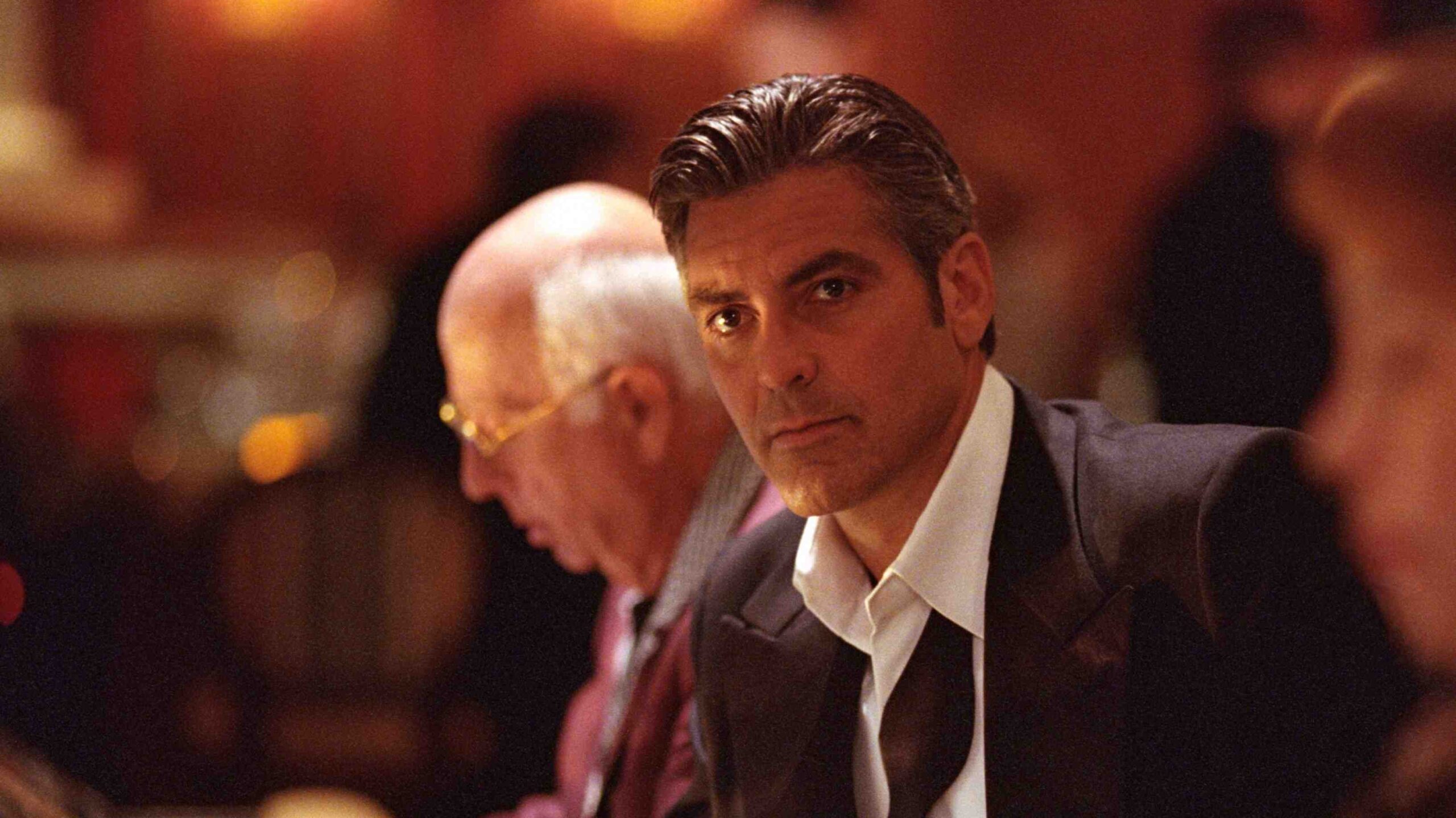Man in a Dark Suit and White Shirt at a Dimly Lit Formal Event Looking Toward the Camera