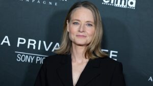 Portrait of a Woman with Blond Hair in a Black Blazer Posing in Front of a Step and repeat Backdrop at an Event