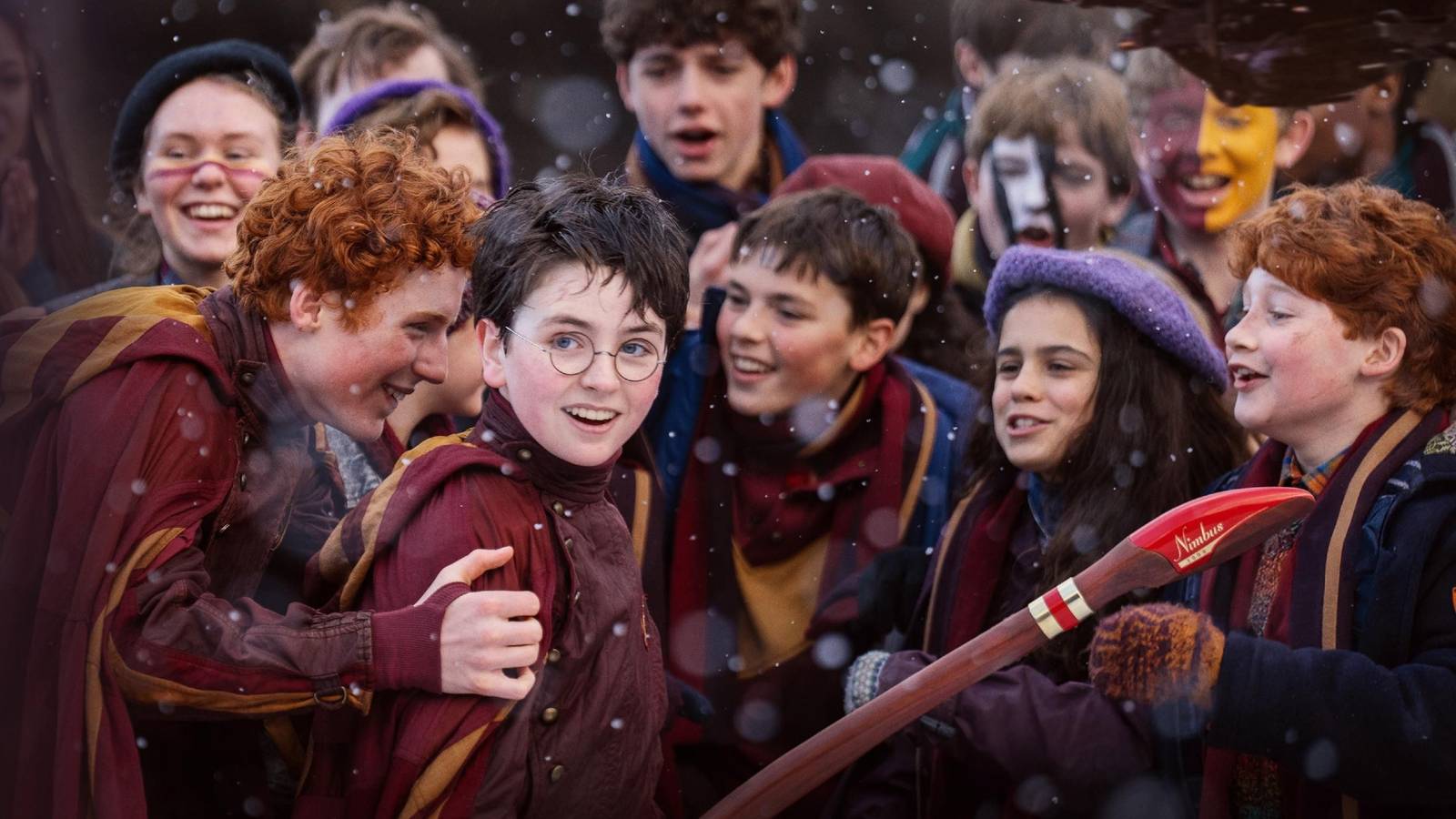 Group of Children in Maroon Robes and Scarves Celebrate Outdoors in Snowfall Around a Long Red Nimbus Broom