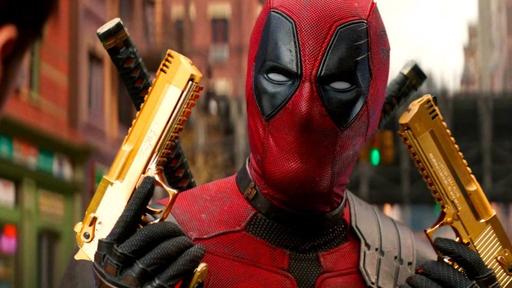 Deadpool in a Red Suit Holds Two Gold Pistols Across His Shoulders in an Urban Setting Facing the Camera