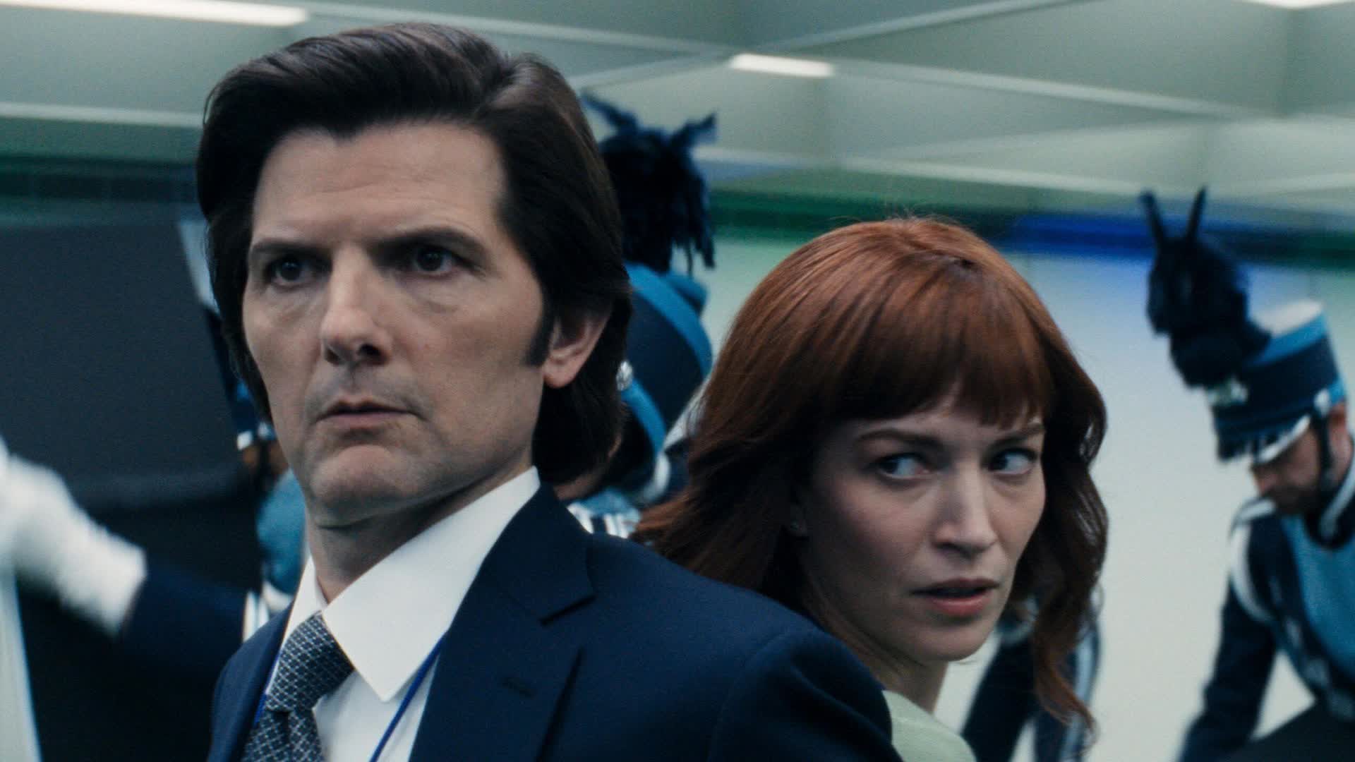 Man in a Navy Suit and Tie Looking to the Left with a Serious Expression in a Crowded Indoor Setting