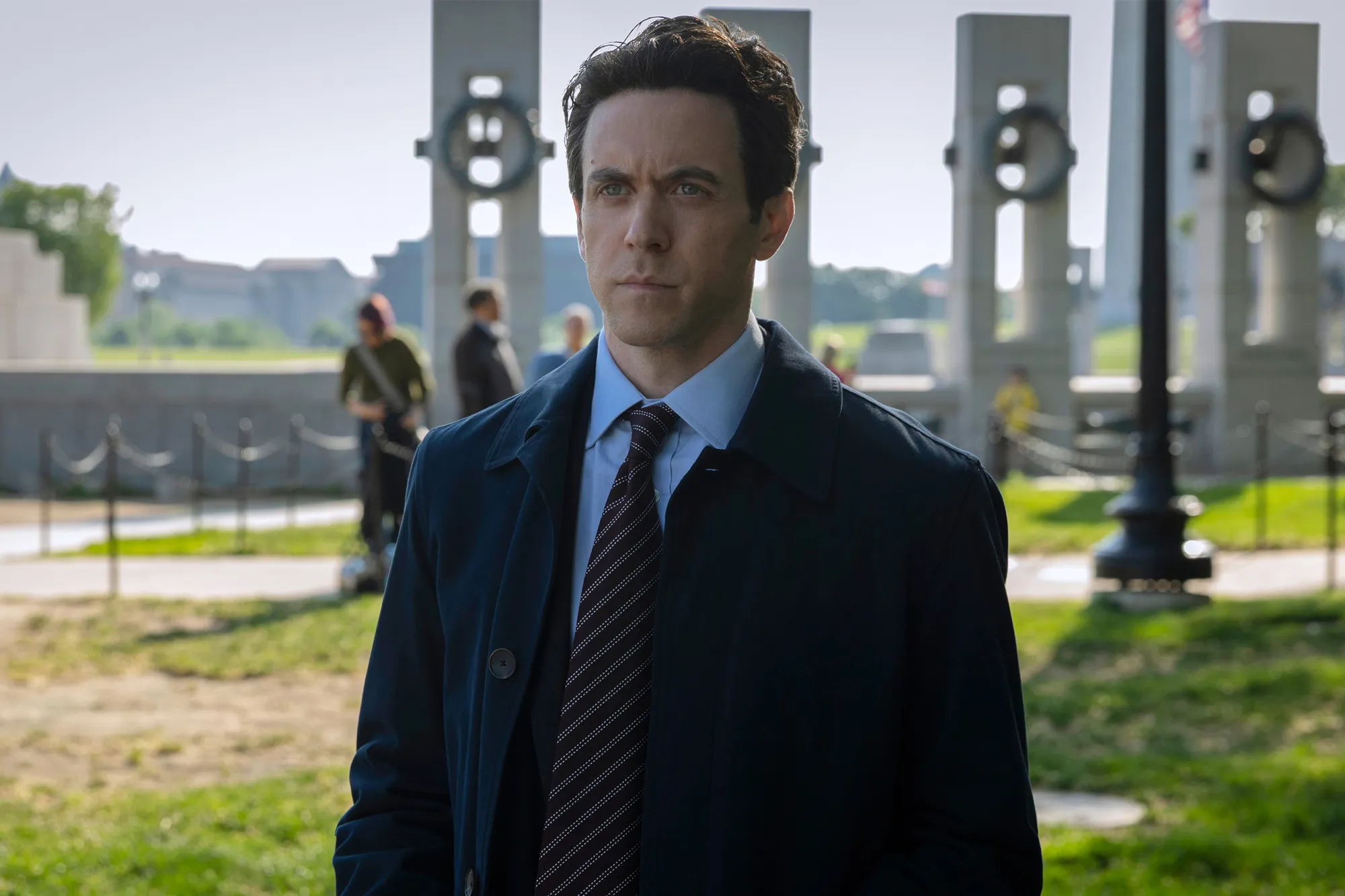 Man in a Navy Coat and Striped Tie Stands Outdoors with Modern Columns in the Background