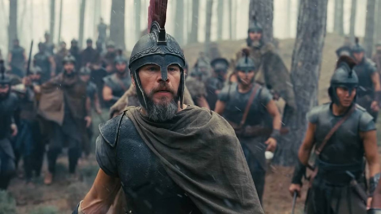 Bearded Warrior in a Metal Helmet and Brown Cloak Leads a Group of Armored Soldiers Through a Forest Battlefield