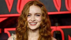 Smiling Young Woman with Long Wavy Red Hair Wearing a Pale Dress Against a Red and Black Backdrop