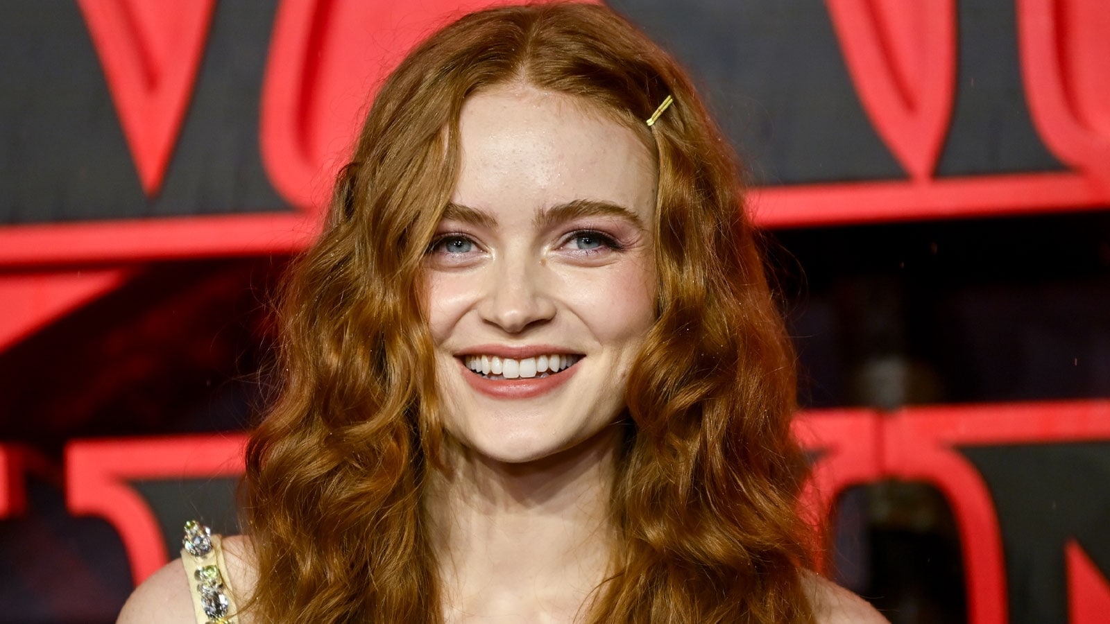 Smiling Young Woman with Long Wavy Red Hair Wearing a Pale Dress Against a Red and Black Backdrop