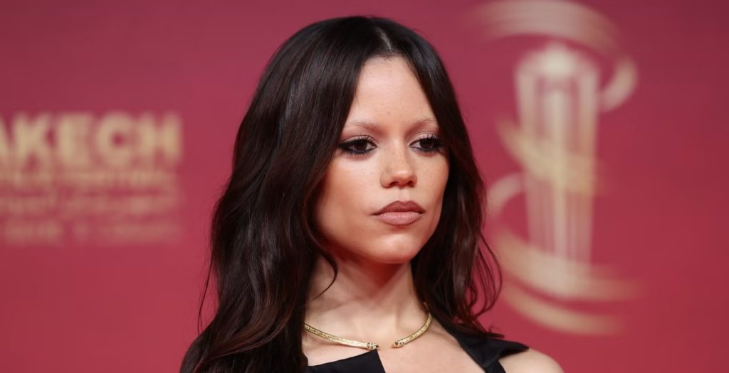 Portrait of a Woman with Long Dark Hair Wearing a Gold Choker Necklace at a Red carpet Event on a Pink Backdrop Looking to the Side