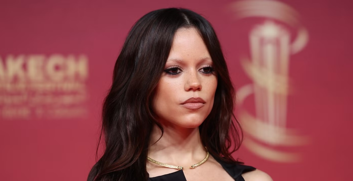 Portrait of a Woman with Long Dark Hair Wearing a Gold Choker Necklace at a Red carpet Event on a Pink Backdrop Looking to the Side