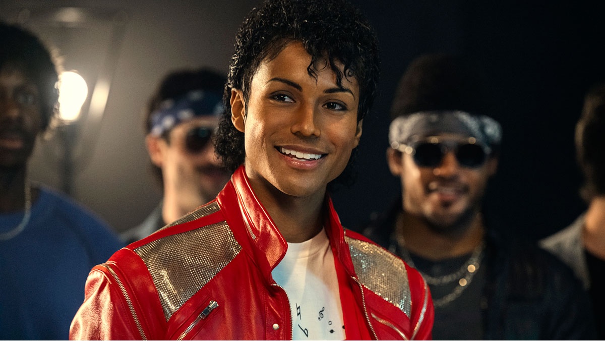 Smiling Performer in a Red Leather Jacket with Silver Shoulder Panels Backstage with Crew in the Background