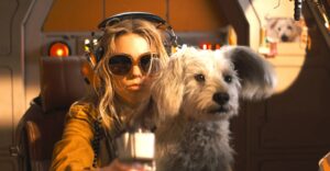 Woman Wearing Oversized Sunglasses and a Headset Sits in a Spacecraft Cockpit with a Fluffy White Dog Beside Her