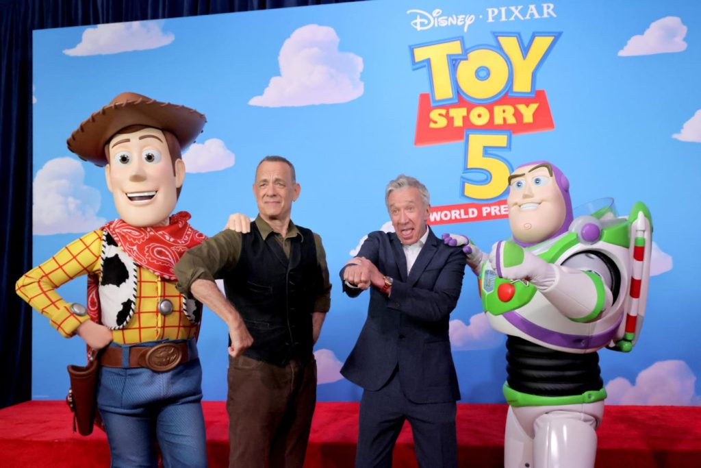 Woody and Buzz Lightyear Mascots Pose with Two Men on a Stage with a Toy Story 5 World Premiere Backdrop