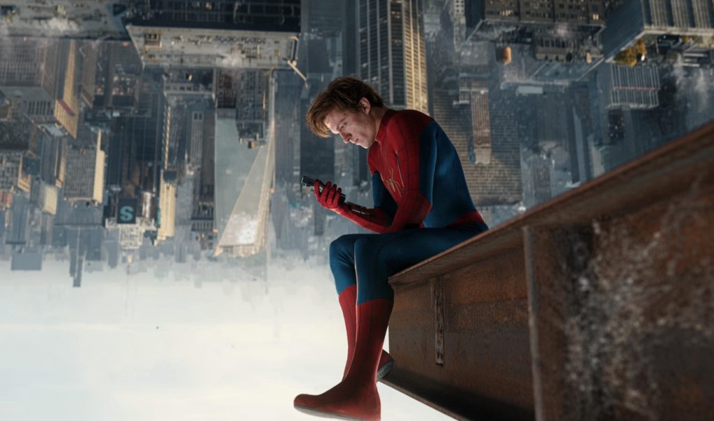 Spider man in His Suit Sits on a Rusted Rooftop Beam Above a City Looking at a Handheld Device