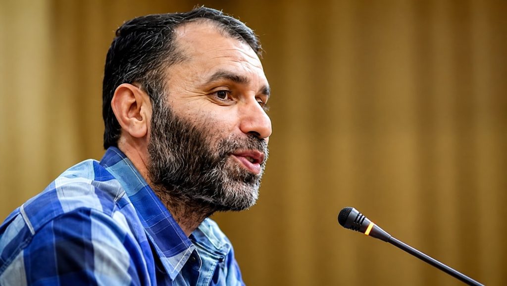 Side Profile of a Bearded Man in a Blue Plaid Shirt Speaking into a Microphone in a Warm toned Room