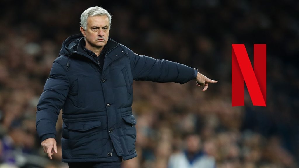 Soccer Manager Jose Mourinho in a Dark Puffer Coat Pointing to the Right with a Large Red Netflix Logo in the Background