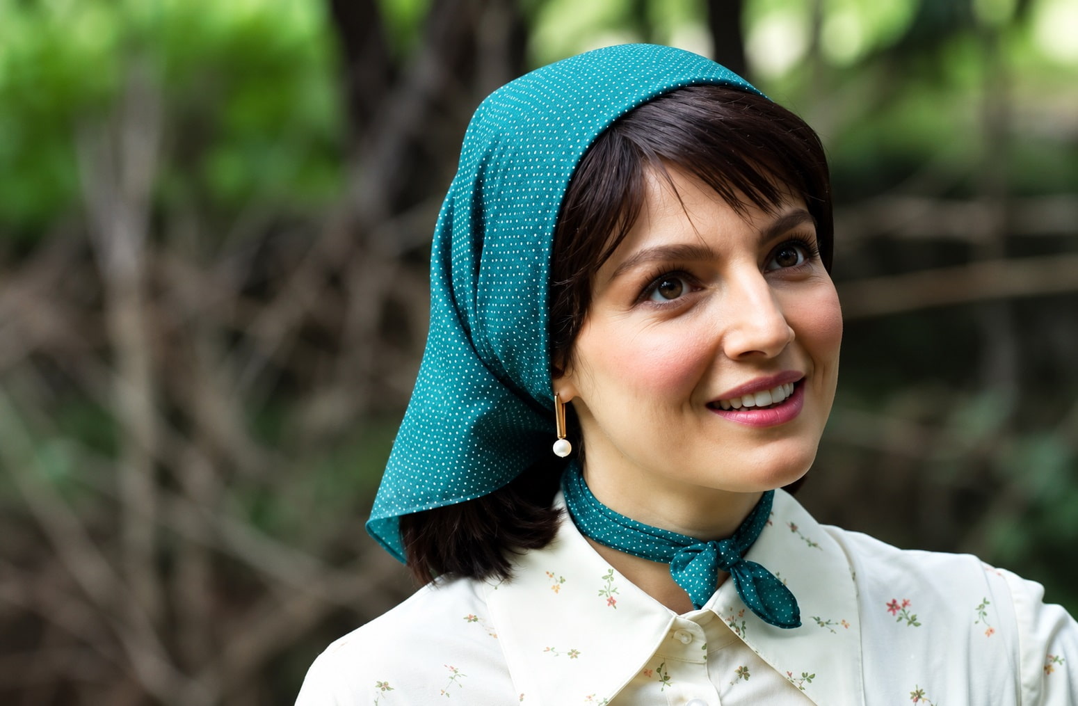 Smiling Woman Outdoors Wearing a Teal Polka dot Headscarf and Matching Neck Scarf Floral Blouse Pearl Drop Earring