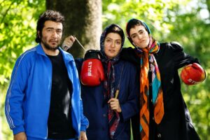 Three Friends Posing in a Sunny Park Two Women Wearing Headscarves Hold Red Boxing Gloves While a Man in a Blue Jacket Stands Beside Them
