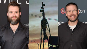 Bearded Man in a Dark Button up Shirt on the Left Central Artwork Featuring a Tall Skeletal Sculpture Against a Sunset and a Bearded Man with Glasses in a Dark Shirt on the Right at Event Photos