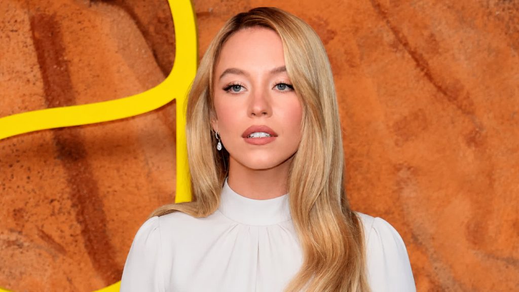 Portrait of a Blonde Woman in a White Blouse Against a Warm Orange Textured Background with a Hint of Yellow Shape Nearby