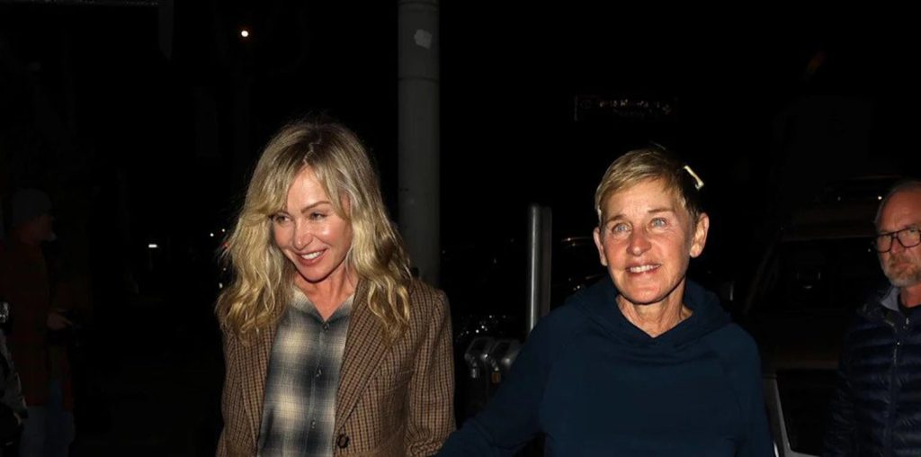 Two Women Walk at Night Smiling the Blonde Wears a Brown Plaid Blazer and the Other a Dark Hoodie