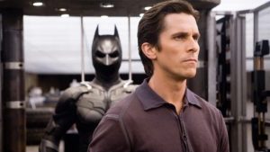 Man in a Brown Polo Shirt in Profile with a Large Batman Statue Behind Him in a Modern Gym